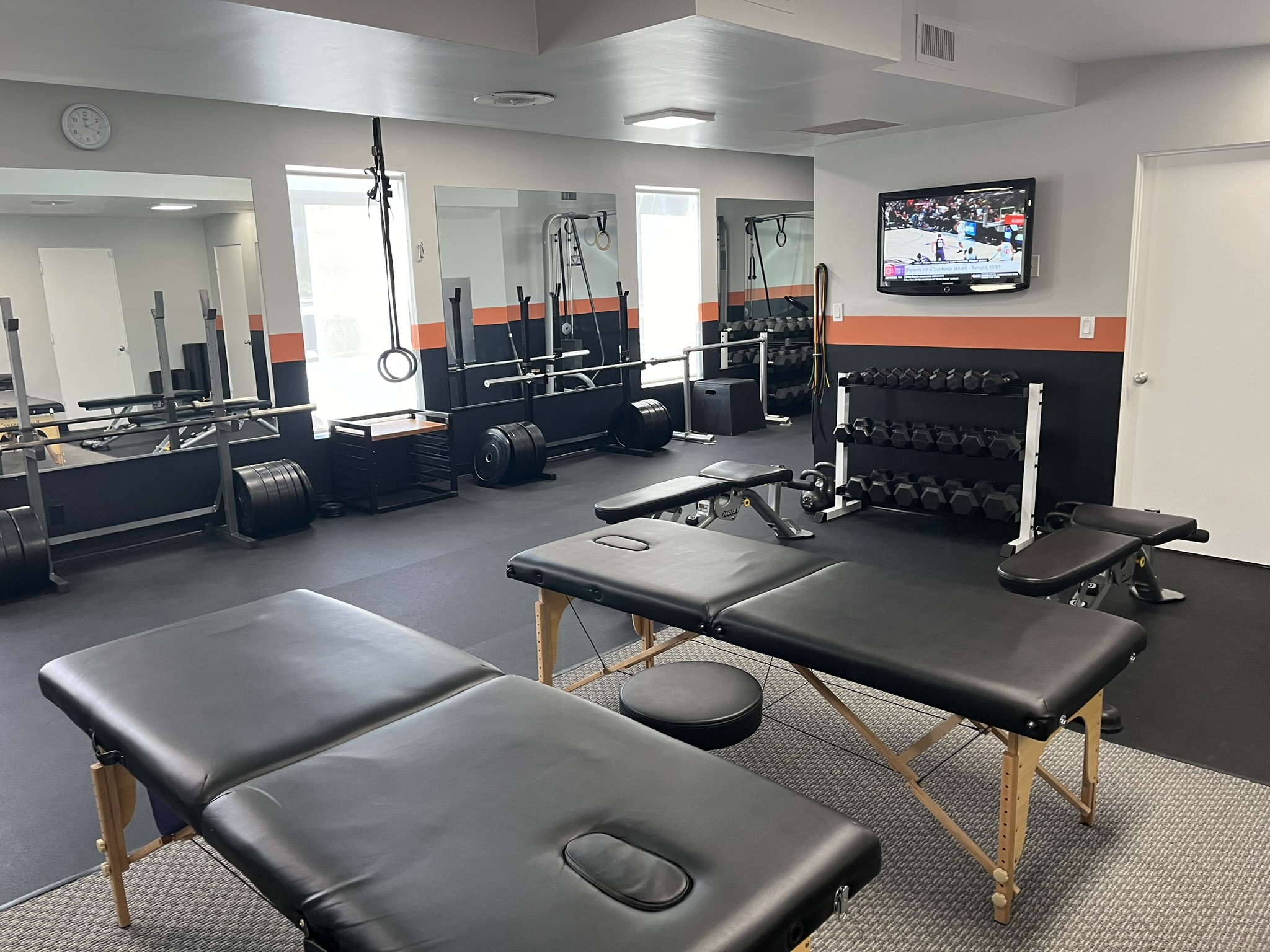 A physical therapy gym with black, white, and orange walls with a variety of workout equipment and weight.